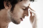 Side view of young man with headache touching forehead on white 